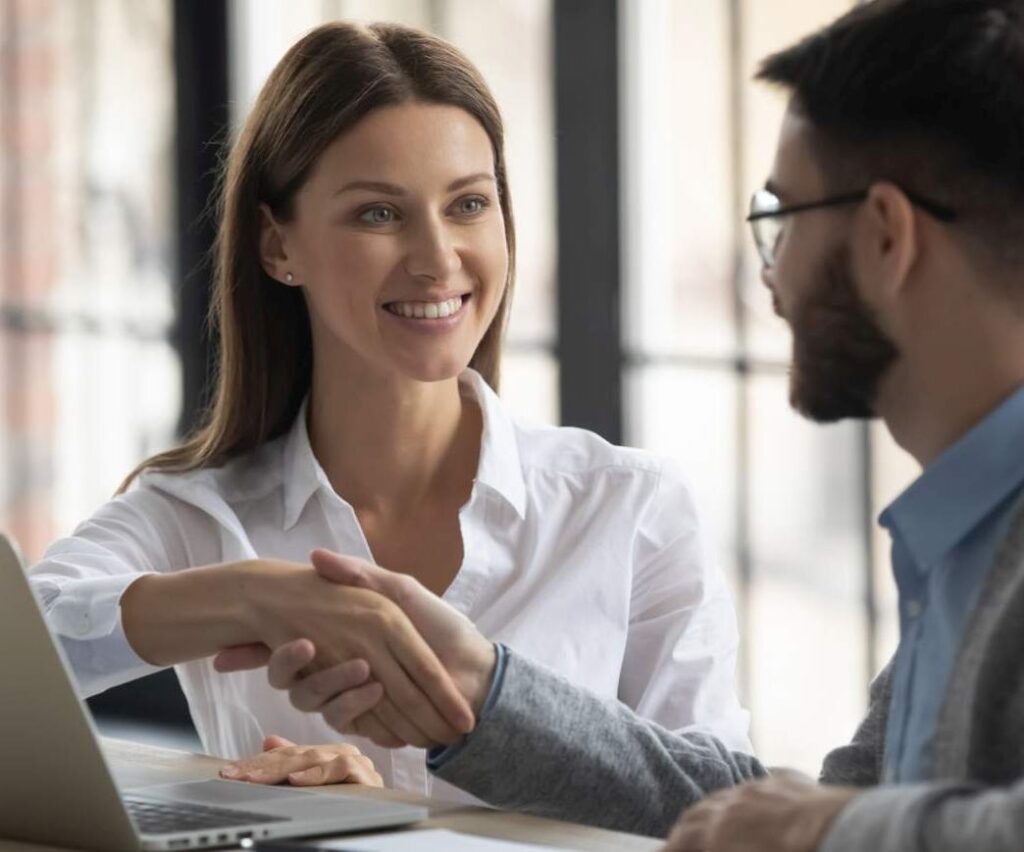 Happy businesswoman shaking hands with man job seeker near laptop.