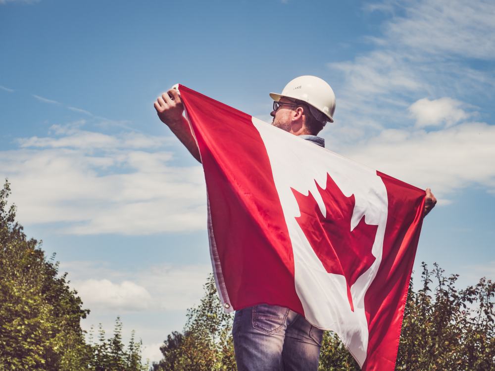 Handsome engineer, holding Canadian Flag in the park against the
