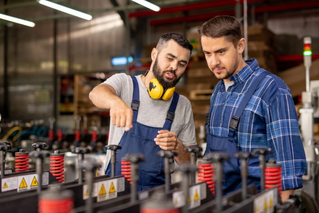 Young trainee looking at industrial equipment while confident manager explaining its working characteristics