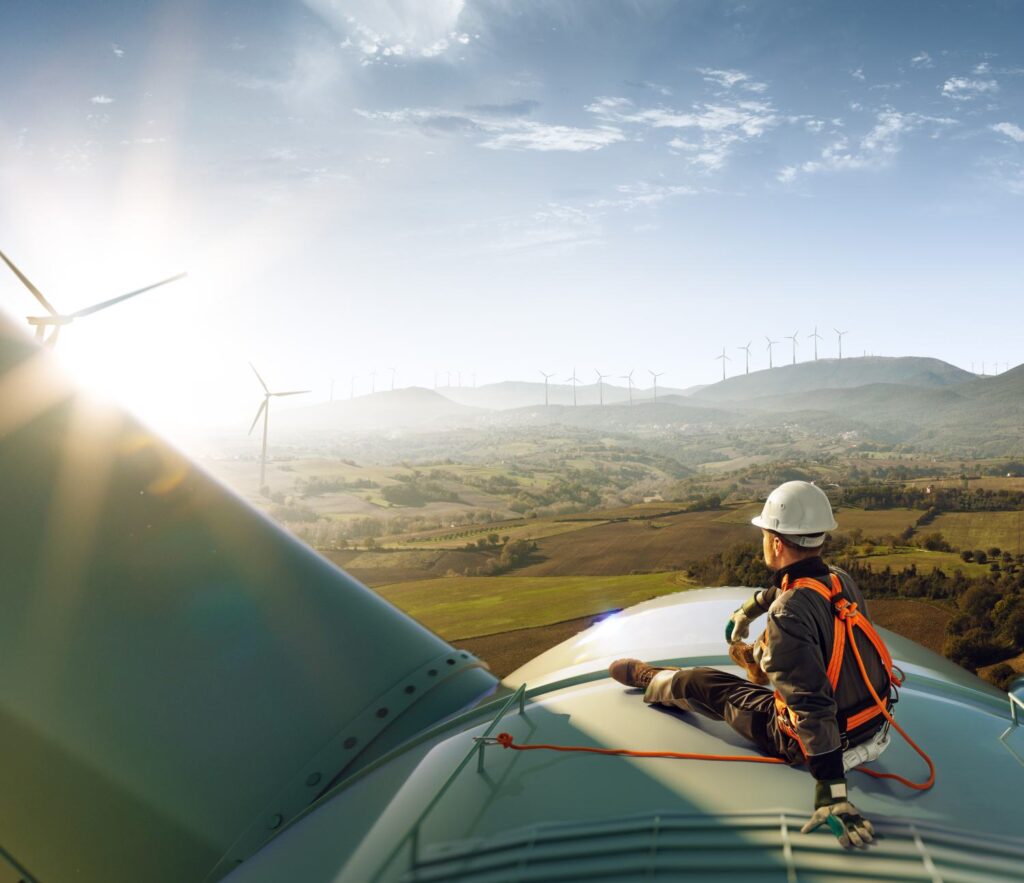Happy engineer feel success after good work. He standing a top of windmill and looking beautiful sunset landscape
