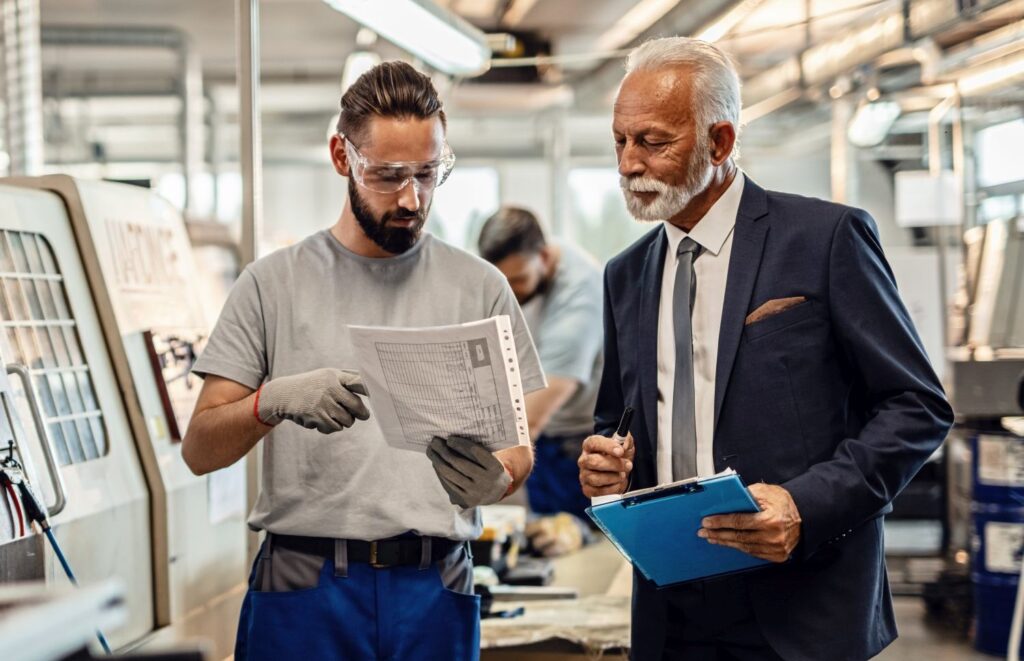 Specialist and senior businessman cooperating while going through paperwork in factory plant.