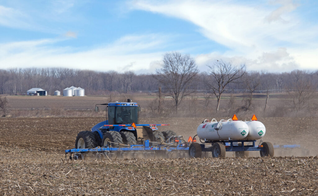 Farm tractor pulling twin NH₃ nurse tanks during field application, showing agricultural use of anhydrous ammonia.