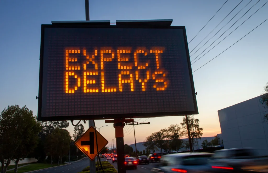 Electronic variable message signs warning drivers to expect delays approaching a work zone at sunset.