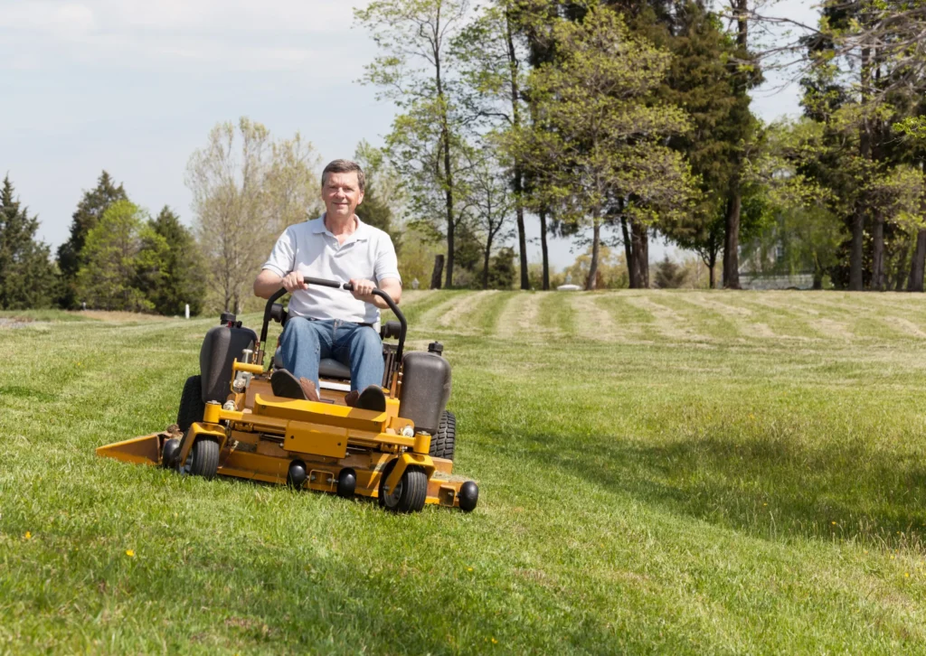Operator driving a ride-on lawnmower across a grassy field during spring mowing.