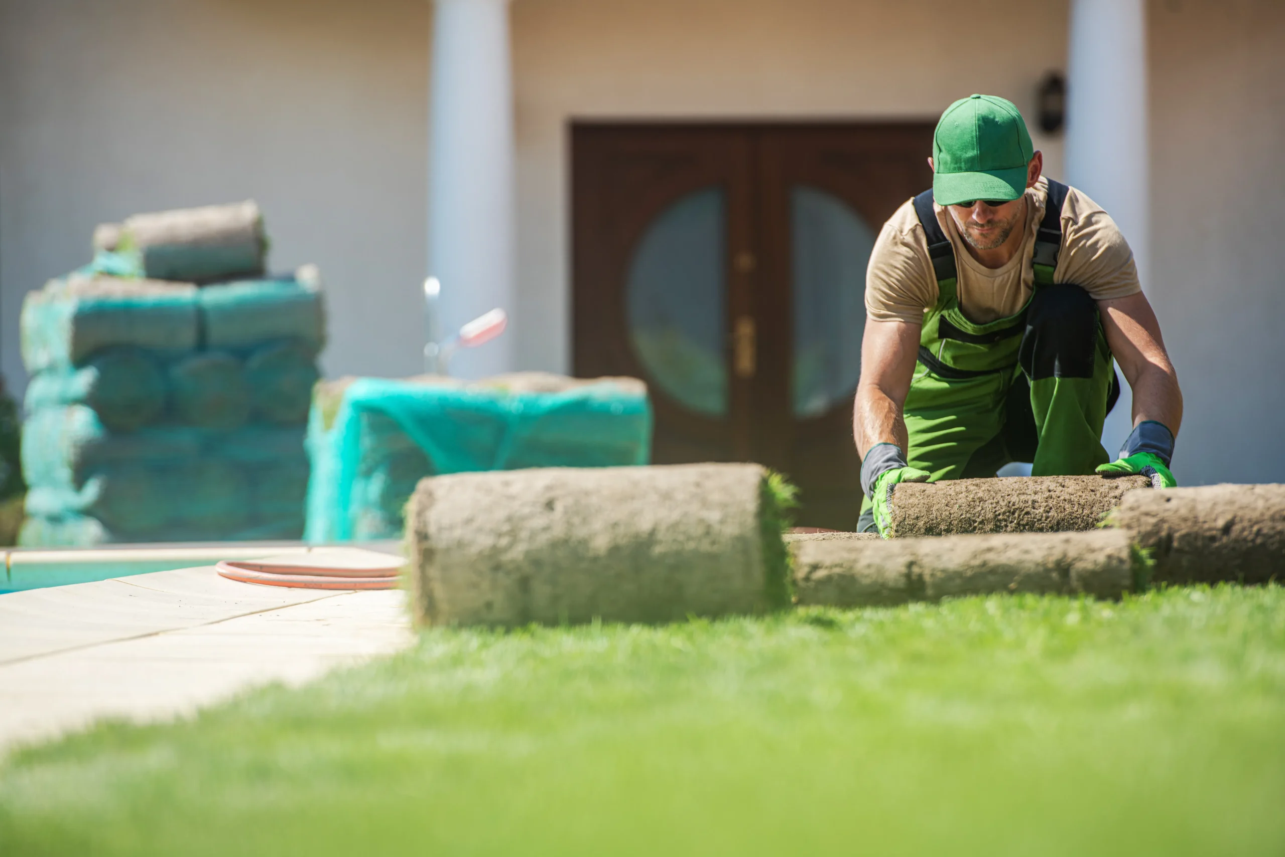 A worker kneeling on grass preparing a chemical sprayer while wearing high-visibility PPE.