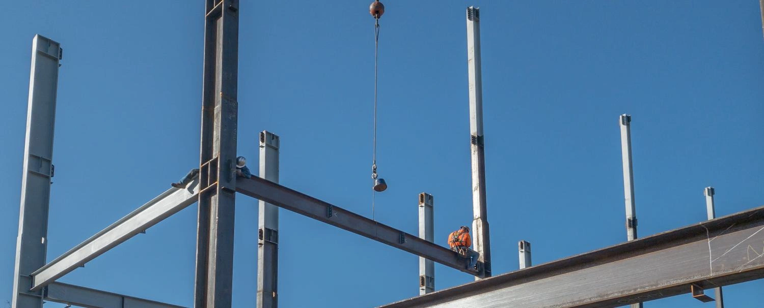 2 ironworkers are on a horizontal steel I-beam just put into pla